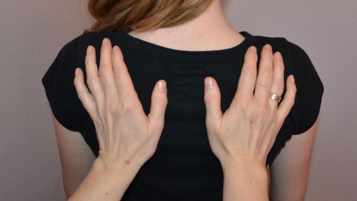 Auf dem Foto sieht man den Rücken einer Frau, auf dem zwei Hände liegen.