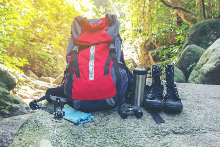 Auf dem Foto sieht man einen Rucksack, ein Fernglas, Wanderschuhe, Trinkflasche, Kompss und ein Handtuch, die auf einem Felsen stehen.