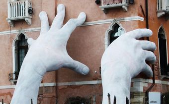 Auf dem Bild sieht man eine Skulptur von Lorenzo Quinn: Zwei riesige Hände, die ein Haus "stützen"